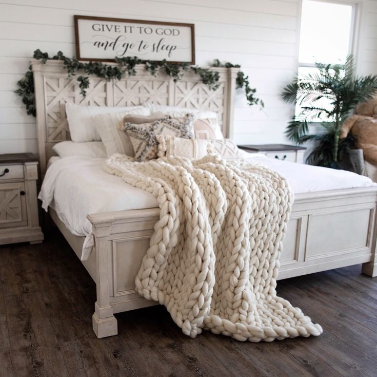Cozy bedroom with a large white bed, chunky knit blanket, and decorative pillows.